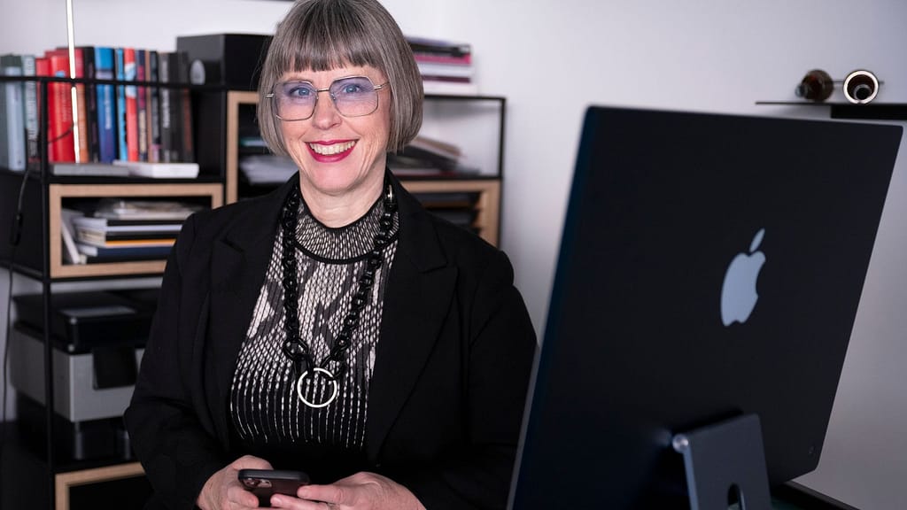 Karin Stehr an ihrem Schreibtisch mit iMac und Handy im Büro